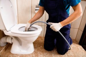 Plumber unclogging blocked toilet with hydro jetting at home bathroom