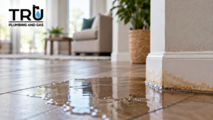 Water pooling across a home’s tile floor near a stained baseboard, illustrating a potential hidden slab leak.